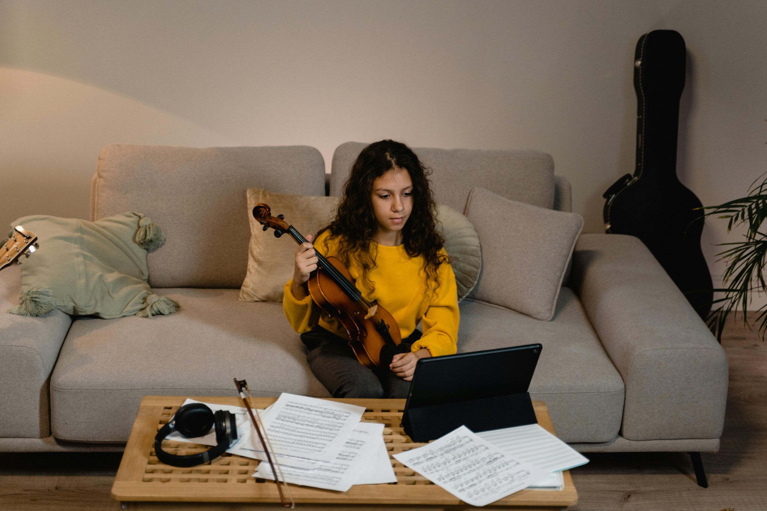 A girl with a violin taking an online music class in a cozy home setting.